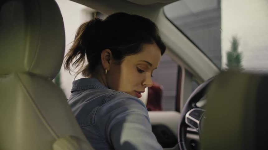 A closeup of a woman sitting in the drivers seat of a car fastening her seatbelt while looking back