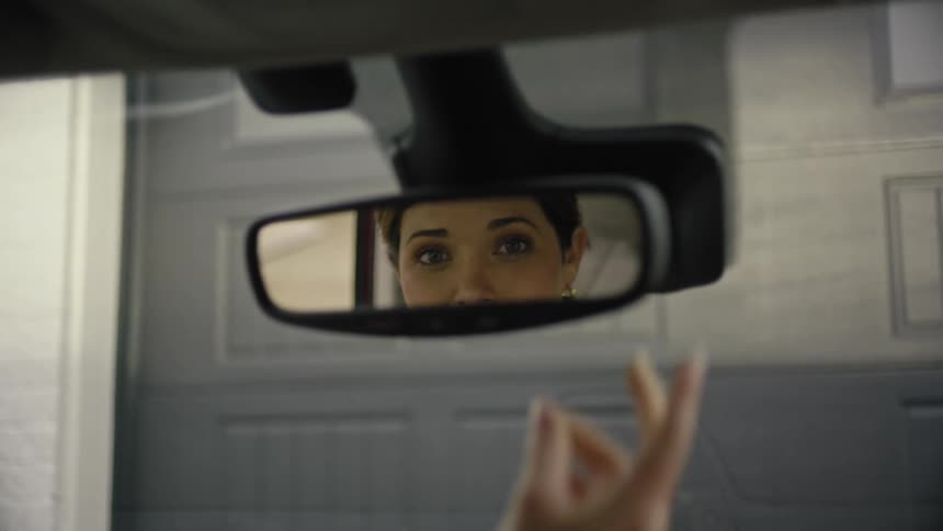 Young woman sitting in an automobile adjusts her rear view mirror