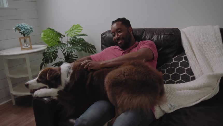 Happy man lying on the couch petting his dog