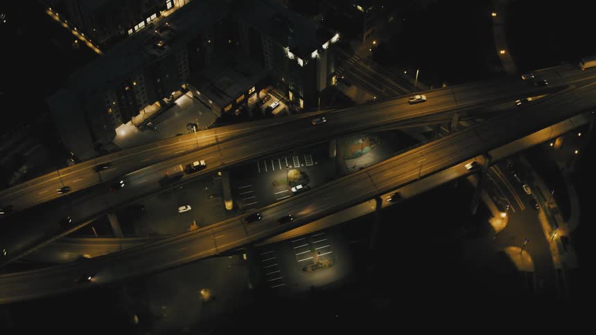 An aerial view of an illuminated highway interchange at night with cars driving along the roads