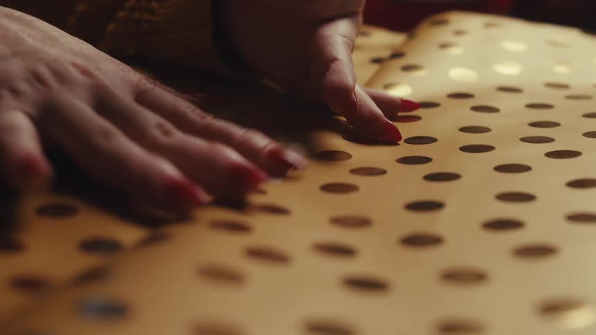 A persons hands with red nails sticking a white masking tape on a yellow paper with black dots