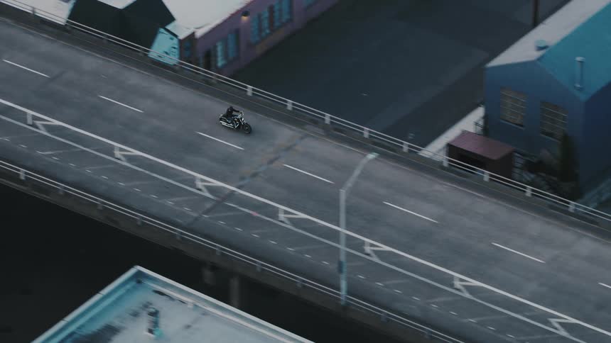 An aerial view shows a motorcycle riding on an elevated highway through an urban area