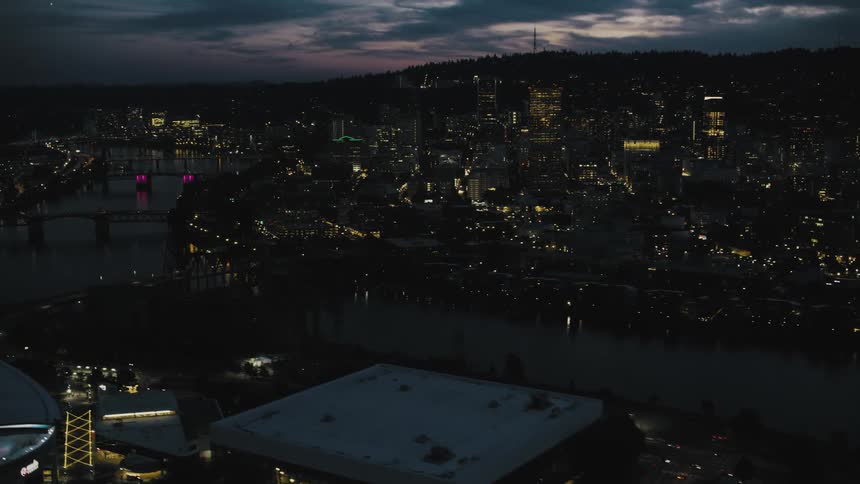 This is a wide nighttime aerial shot of a city with a river running through it numerous lit buildings and several illuminated bridges