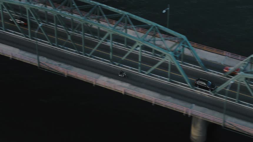 A motorcycle driving down a street from a suspension bridge over a body of water