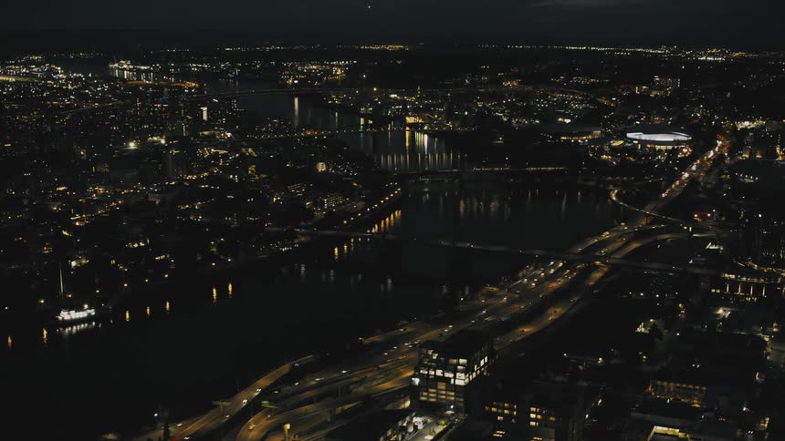 An aerial view of a city at night with illuminated roads buildings and a body of water in the distance