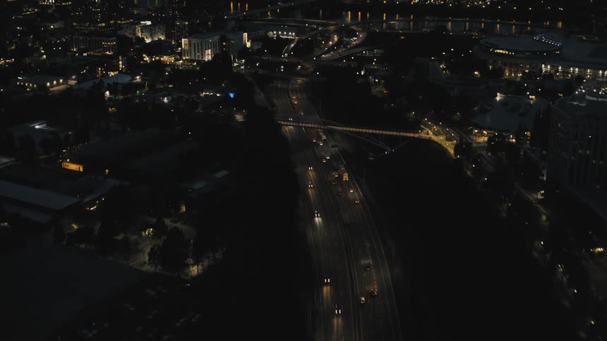 An aerial view of a city at night with illuminated roads buildings and a body of water in the distance