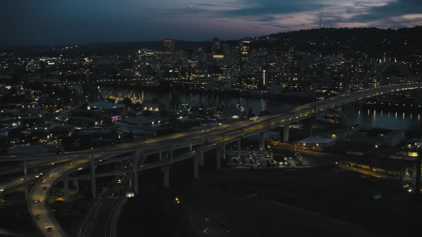 The city of portland oregon is illuminated at night with bridges spanning the river and traffic flowing along the highways