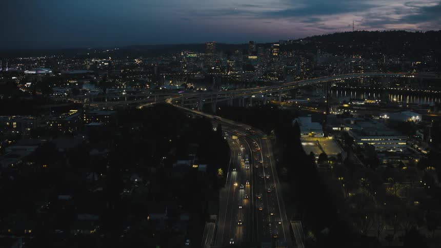 An aerial view of a city at night with illuminated roads buildings and a body of water in the distance