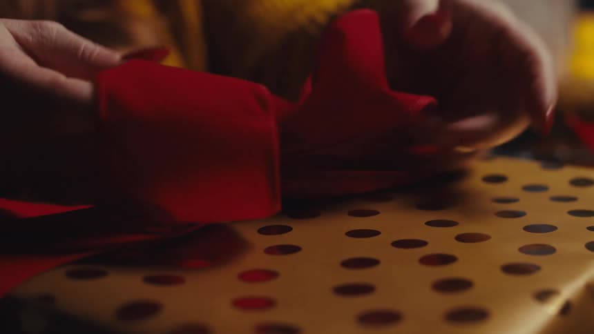 Pair of hands finishing a red bow on a gift box