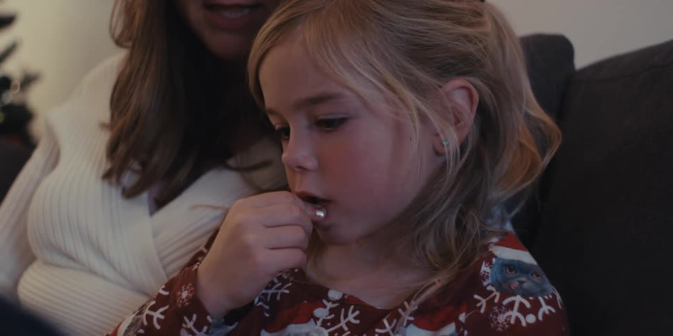 A mother and daughter in a festive red shirt with reindeer and snowflakes read a storybook together on the couch