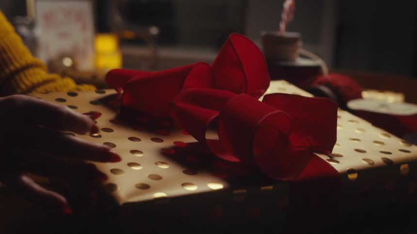 A womans hands are holding a wrapped christmas gift in her living room