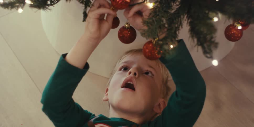 Boy lying on the floor and placing red balls on a christmas tree