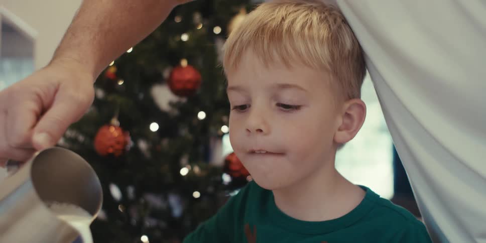 Father pouring milk into mug for his little boy son who is sitting at table