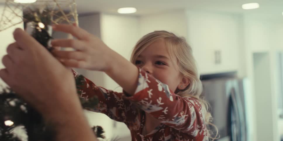 Happy girl placing a star on top of a christmas tree