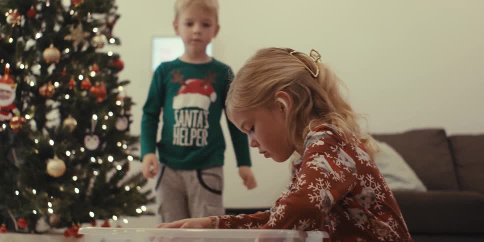 Children decorating a christmas tree with ornaments at home