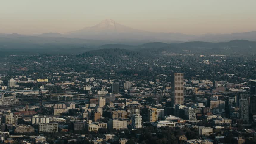 A panoramic view captures the cityscape of portland oregon with the willamette river snaking through its heart and mount hood looming in the distance