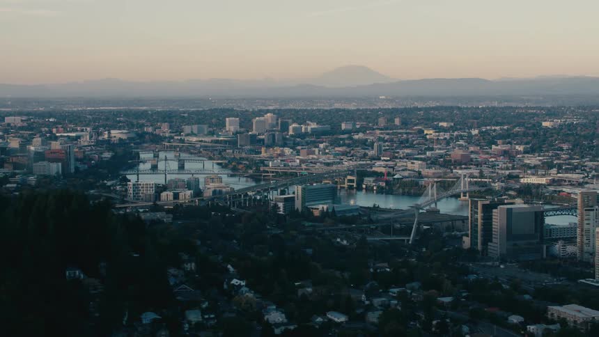 A panoramic view of the cityscape of portland oregon with the willamette river snaking through its heart and mount hood looming in the distance