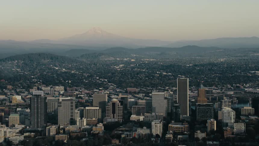 A panoramic view of a city skyline at dusk with a mountain in the distance