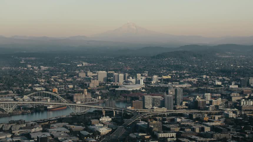 A panoramic view captures the cityscape of portland oregon with the willamette river snaking through its heart and mount hood looming in the distance
