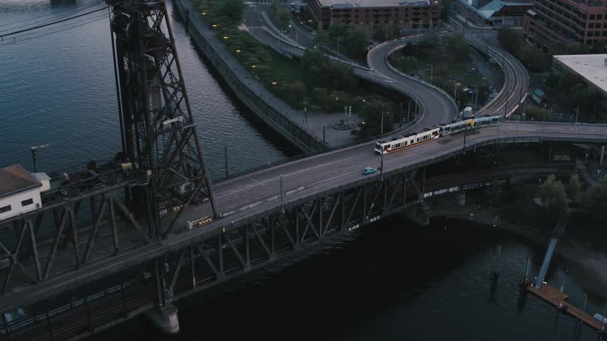 Aerial view of a train and vehicles passing over a sea canal viaduct through the city