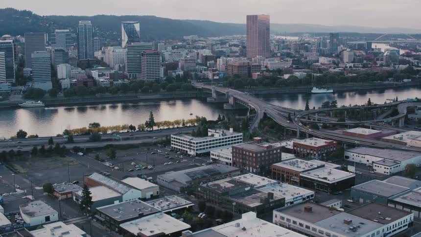 An aerial view captures portland oregon with its cityscape a river with a boat bridges and surrounding landscape on a cloudy day