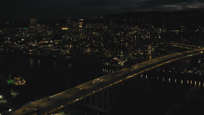 An aerial view of a huge suspension bridge over the water with several cars passing over it at night