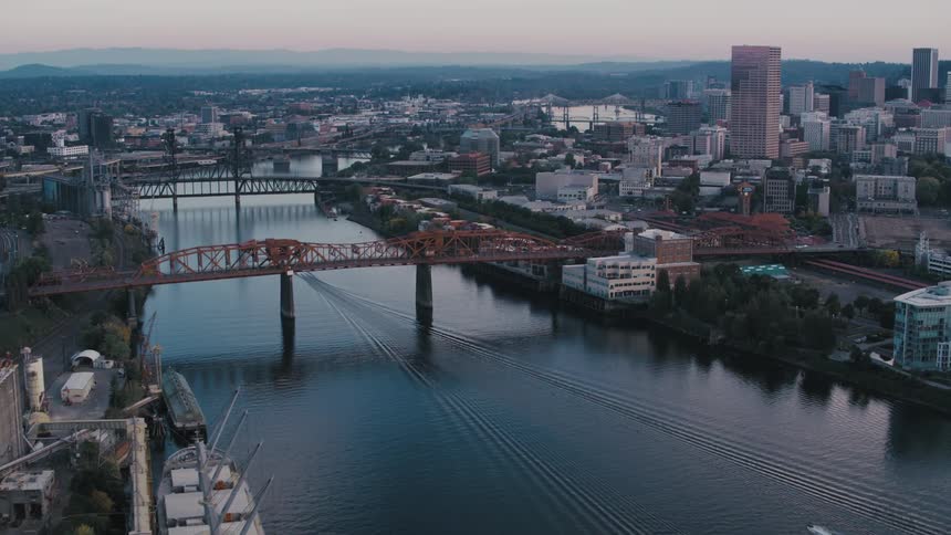 A cargo ship navigates the willamette river passing under multiple bridges against the backdrop of the portland skyline