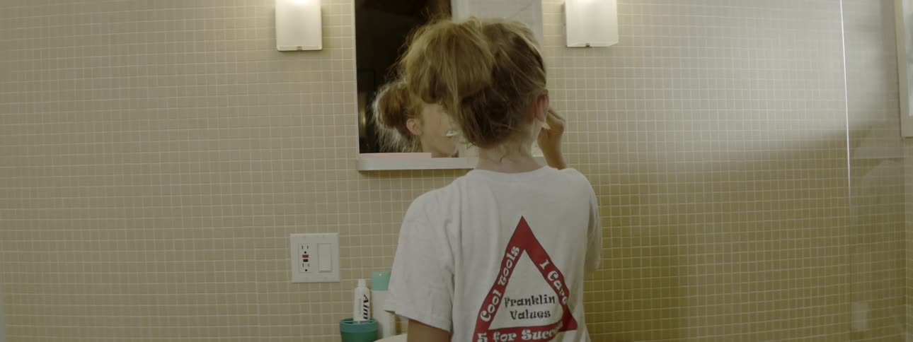 Girl looks in the bathroom mirror while brushing her teeth
