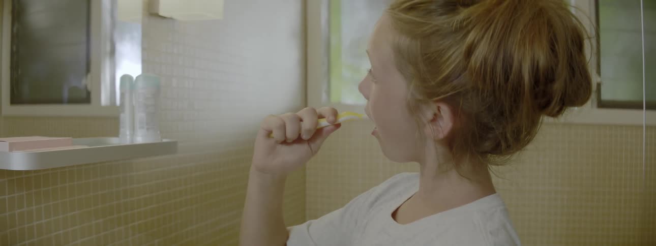 A child brushes her teeth and looks in the mirror