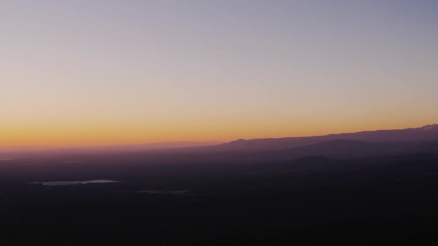Silhouettes of mountains across the landscape under a hazy orange sunset sky