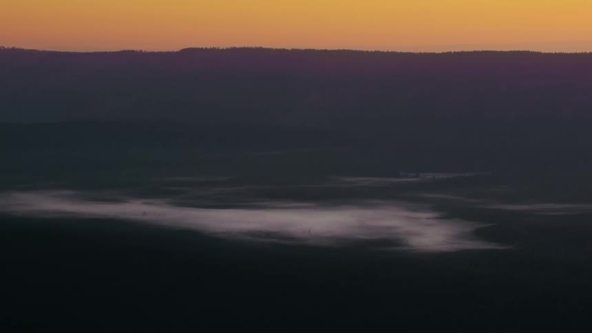 Serene landscape at dawn with layers of dark mountains on the horizon and an orange sky