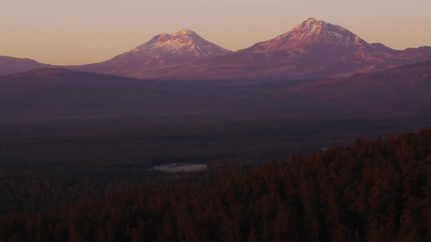 Forested mountain slope and valley with a building and mountains in the distance