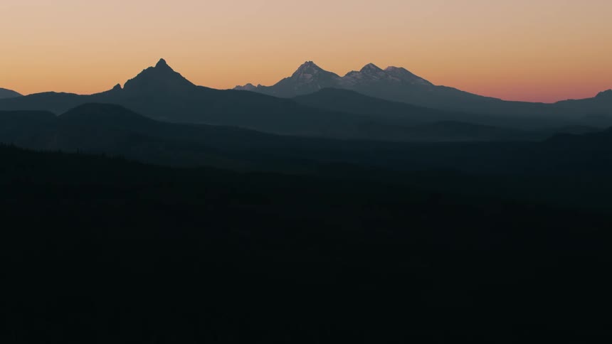 The silhouettes of several mountain peaks stand out against a vibrant orange and pink sunset sky