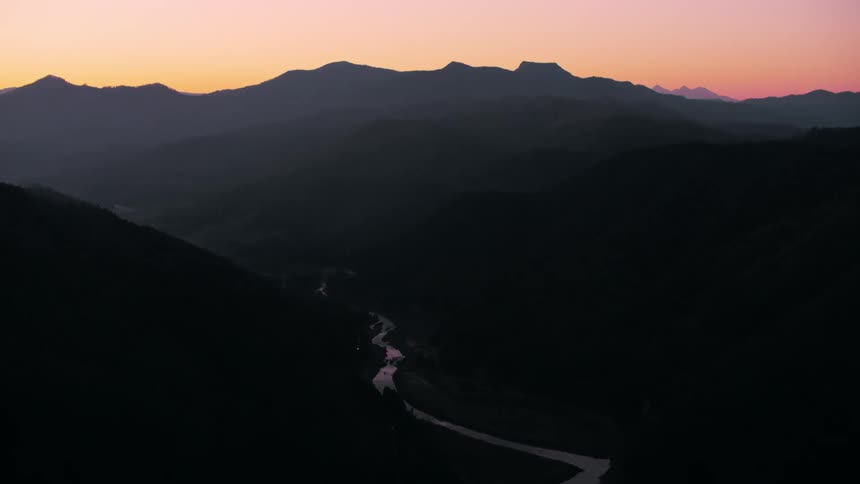 A river winds its way through a dark mountainous valley at dusk with the last rays of sunlight reflecting on the water