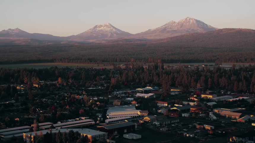 A small town nestled amongst a range of snowcapped mountains is bathed in the warm glow of the setting sun
