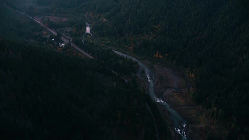 A river winding through a dark forested valley alongside a road and railroad tracks