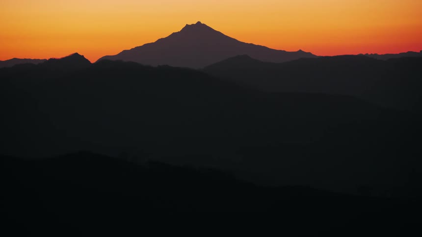 Silhouettes of mountains under an orange sunset sky