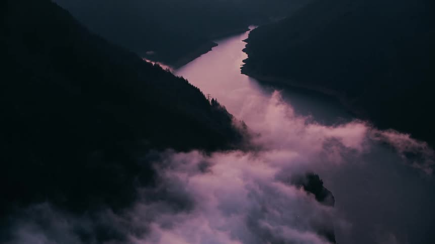 A river snaking through a valley with the silhouettes of the surrounding mountains dramatically outlined against the mist