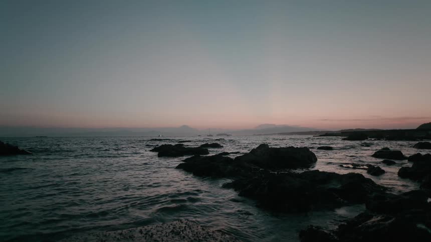 Rocks along the coast as waves roll into shore at dusk