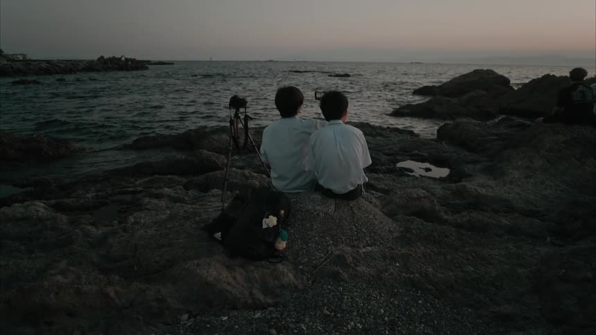 A clip of two teenagers sitting by the sea shore