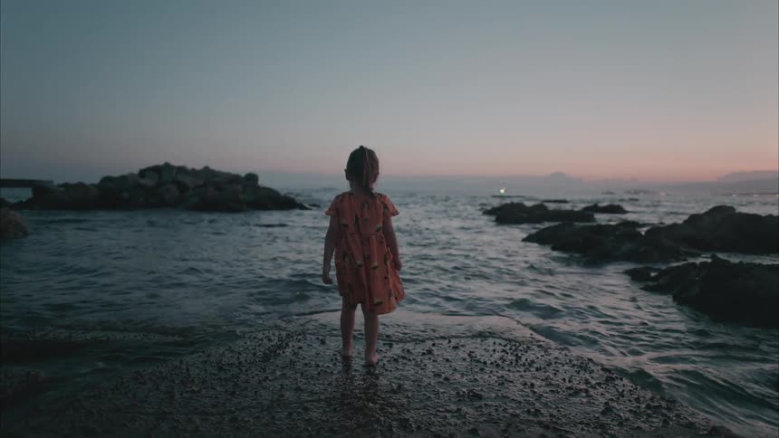 A child walks on a large rock on the shore