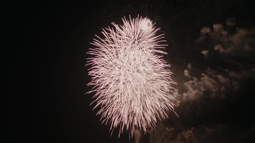 Red fireworks exploding in a night sky and releasing smoke