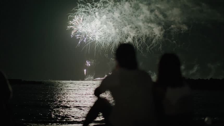People sitting by the sea watching fireworks
