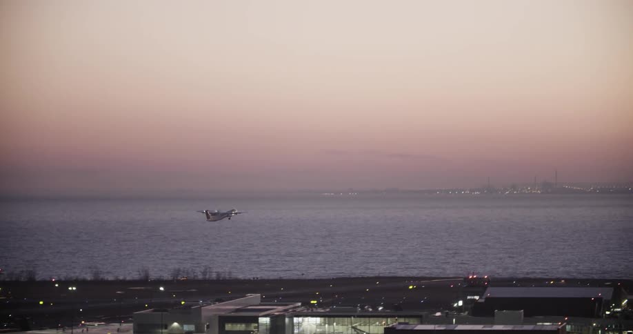 A plane is taking off from a runway near a bay at dusk