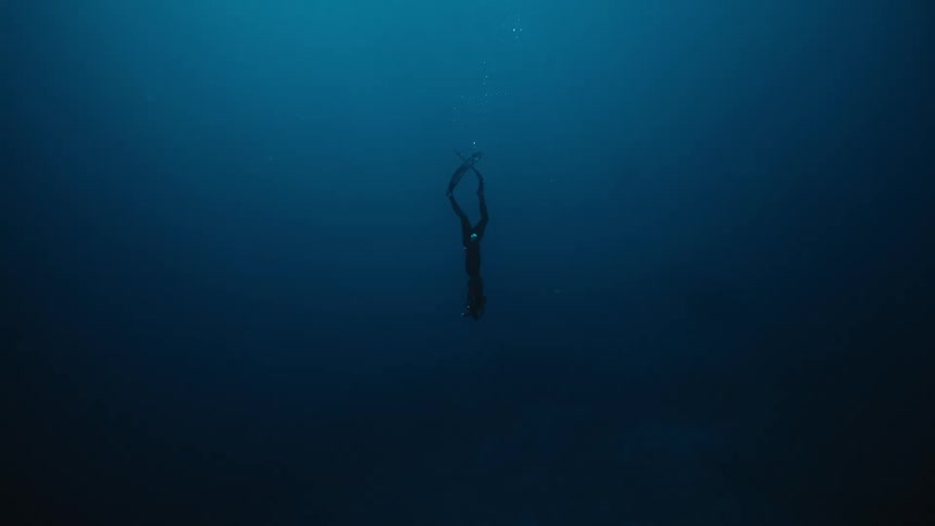 A free diver descends vertically into deep dark ocean waters with their fins visible