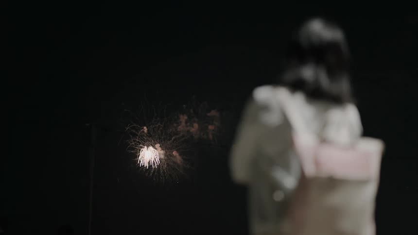Woman watching fireworks glow as they explode in the night sky