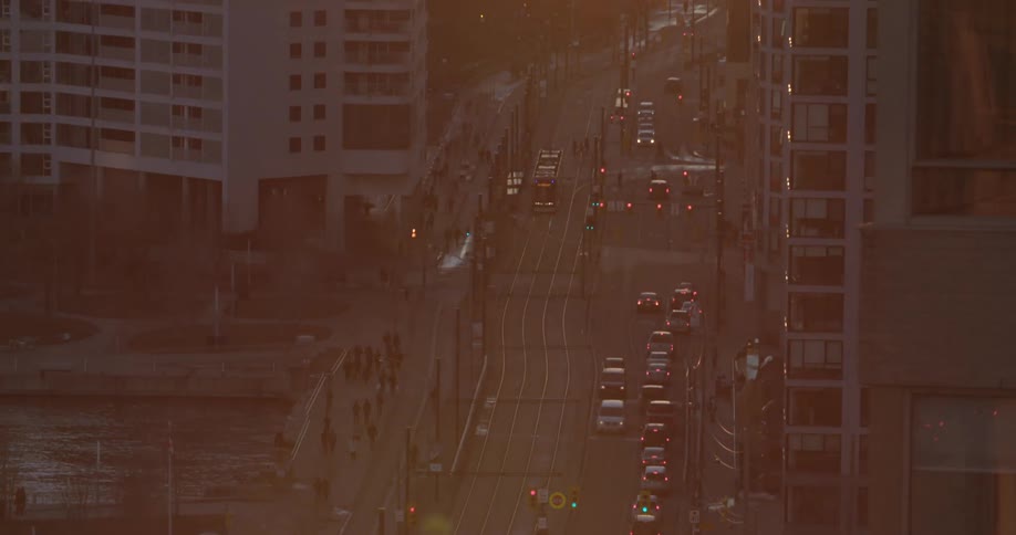 Cars and people are traversing a street in a city at dusk
