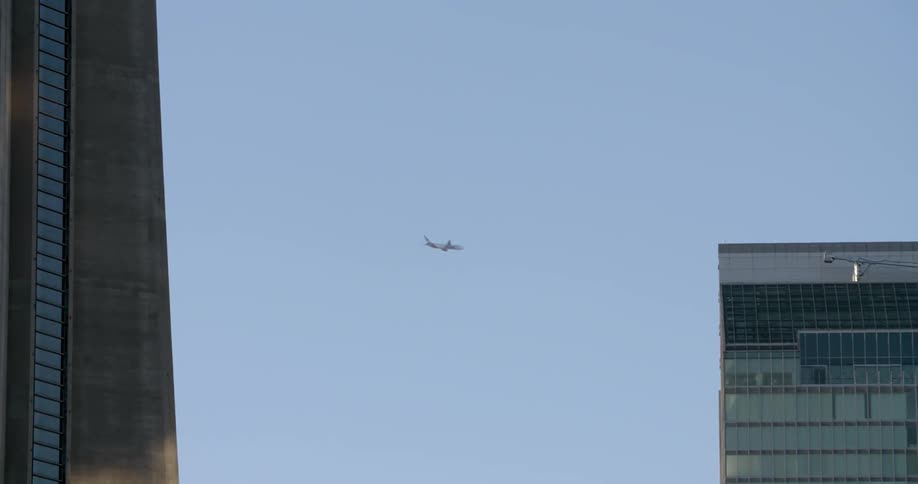 A plane flies in the clear sky behind the building