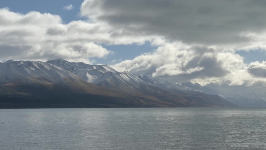 A view across a body of water of snow-capped mountains under a cloudy sky
