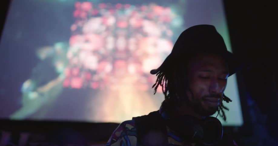 Dj dances while working in a night club near a digital screen
